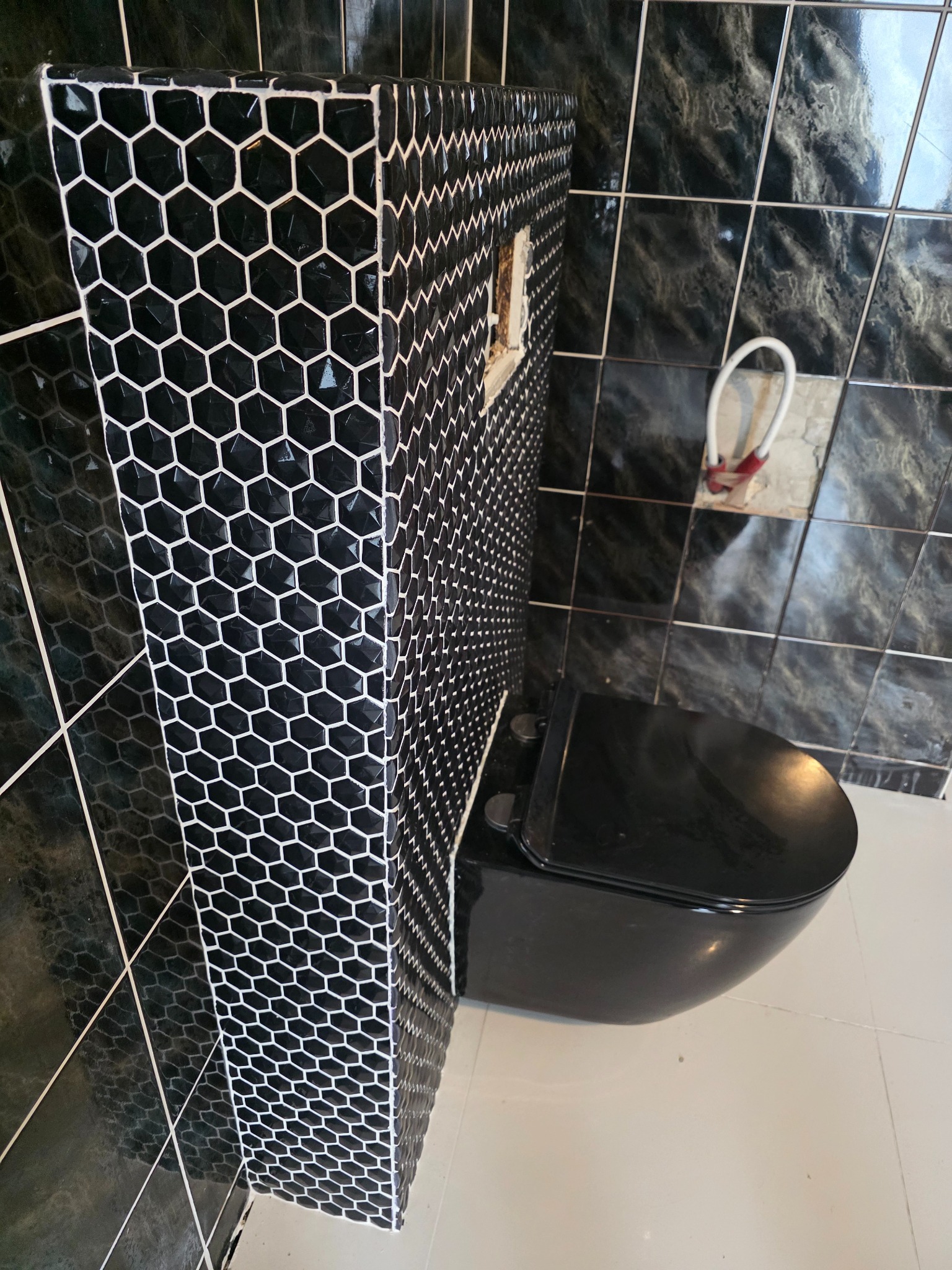 Wykończona toaleta w czarnych heksagonalnych płytkach z białymi fugami, czarna miska WC, marmurowe płytki na ścianach. Nowoczesny design łazienki.