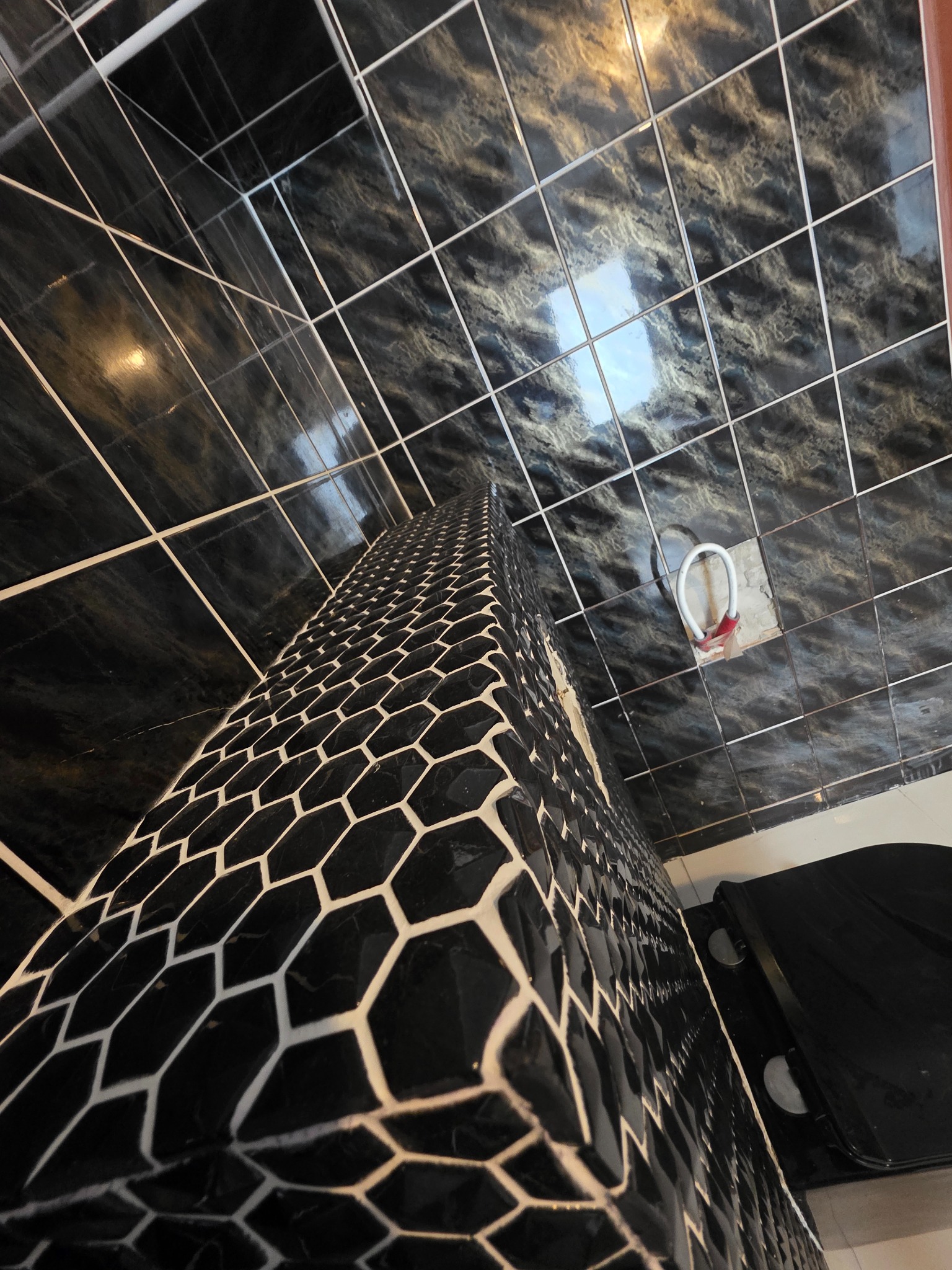 Czarne płytki heksagonalne na obudowie, marmurowe płytki na podłodze i ścianach łazienki. Nietypowy kąt ujęcia podkreśla wzór i fakturę materiałów.