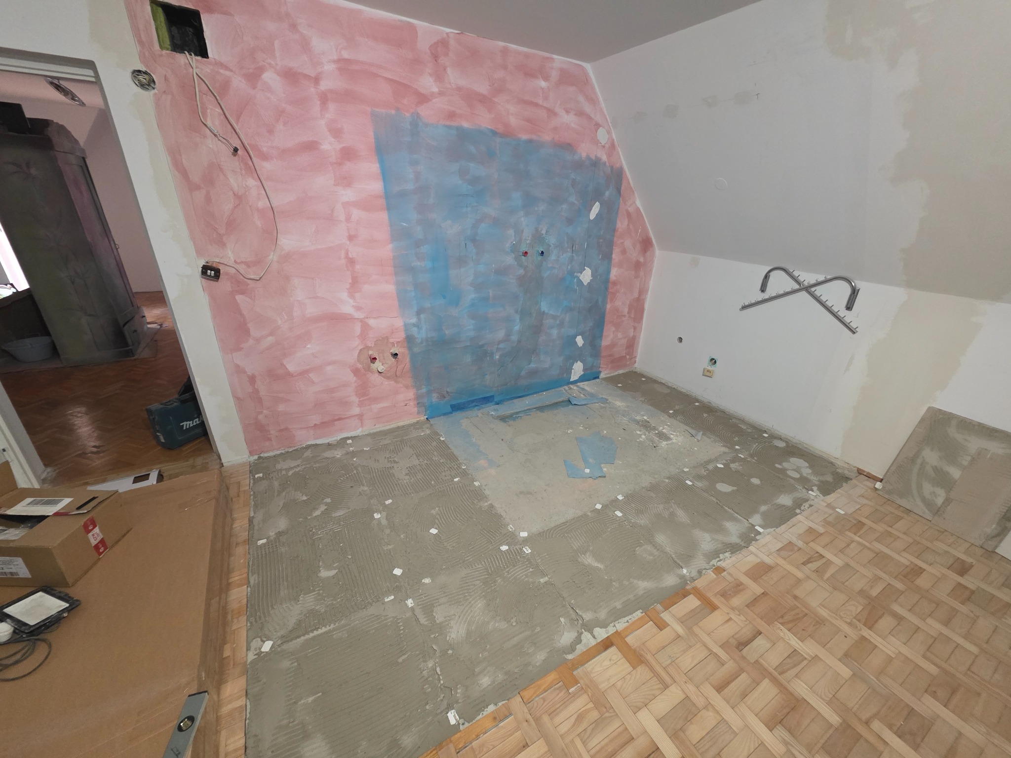 Remont pokoju na poddaszu: przygotowanie podłoża pod płytki, częściowo ułożony parkiet, ściany po gruntowaniu, widoczne instalacje. Etap prac wykończeniowych.