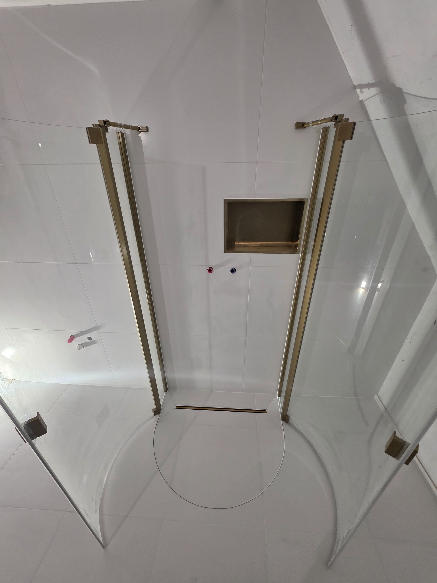 Nowoczesna kabina prysznicowa z elementami w kolorze złotym, białe płytki na ścianach i podłodze, wnęka w ścianie. Minimalistyczny design łazienki po remoncie.