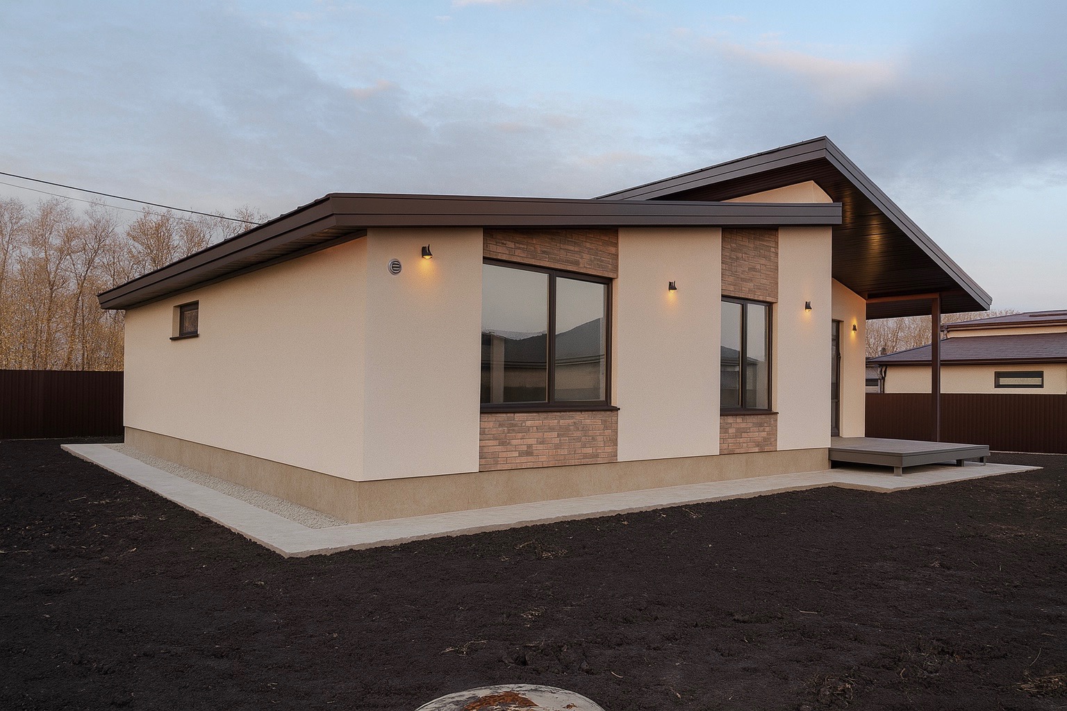 Elewacja domu jednorodzinnego z tynkiem w kolorze kremowym, fragmentami wykończonymi cegłą klinkierową. Widoczne oświetlenie zewnętrzne i ciemny dach.