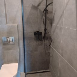 Firma Remontowo- Budowlana Easy Spray Tomasz Dziubanowski - Nowoczesna łazienka z szarymi płytkami, czarną armaturą prysznicową i podtynkową toaletą. Minimalistyczny design z akcentem na funkcjonalność i stonowaną kolorystykę.