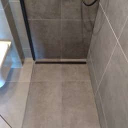 Firma Remontowo- Budowlana Easy Spray Tomasz Dziubanowski - Nowoczesna łazienka z szarymi płytkami, widoczny odpływ liniowy i fragment kabiny prysznicowej. Minimalistyczny design, stonowana kolorystyka.