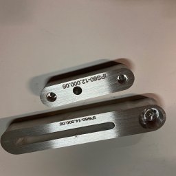 extremePROJECT Alicja Świerczyńska - Dwa metalowe elementy z wywierconymi otworami i wygrawerowanymi numerami seryjnymi, leżące na jasnej powierzchni.