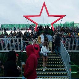 extremePROJECT Alicja Świerczyńska - Widok na schody metalowe z barierkami prowadzące do trybuny z dużą grupą ludzi, nad którą góruje czerwona gwiazda, Warszawa.