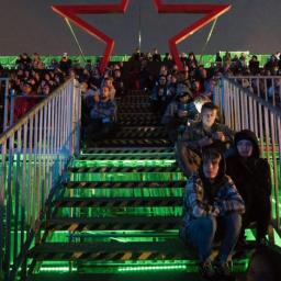 extremePROJECT Alicja Świerczyńska - Metalowe schody z podświetleniem LED prowadzące do platformy z czerwoną gwiazdą, na schodach siedzą ludzie.