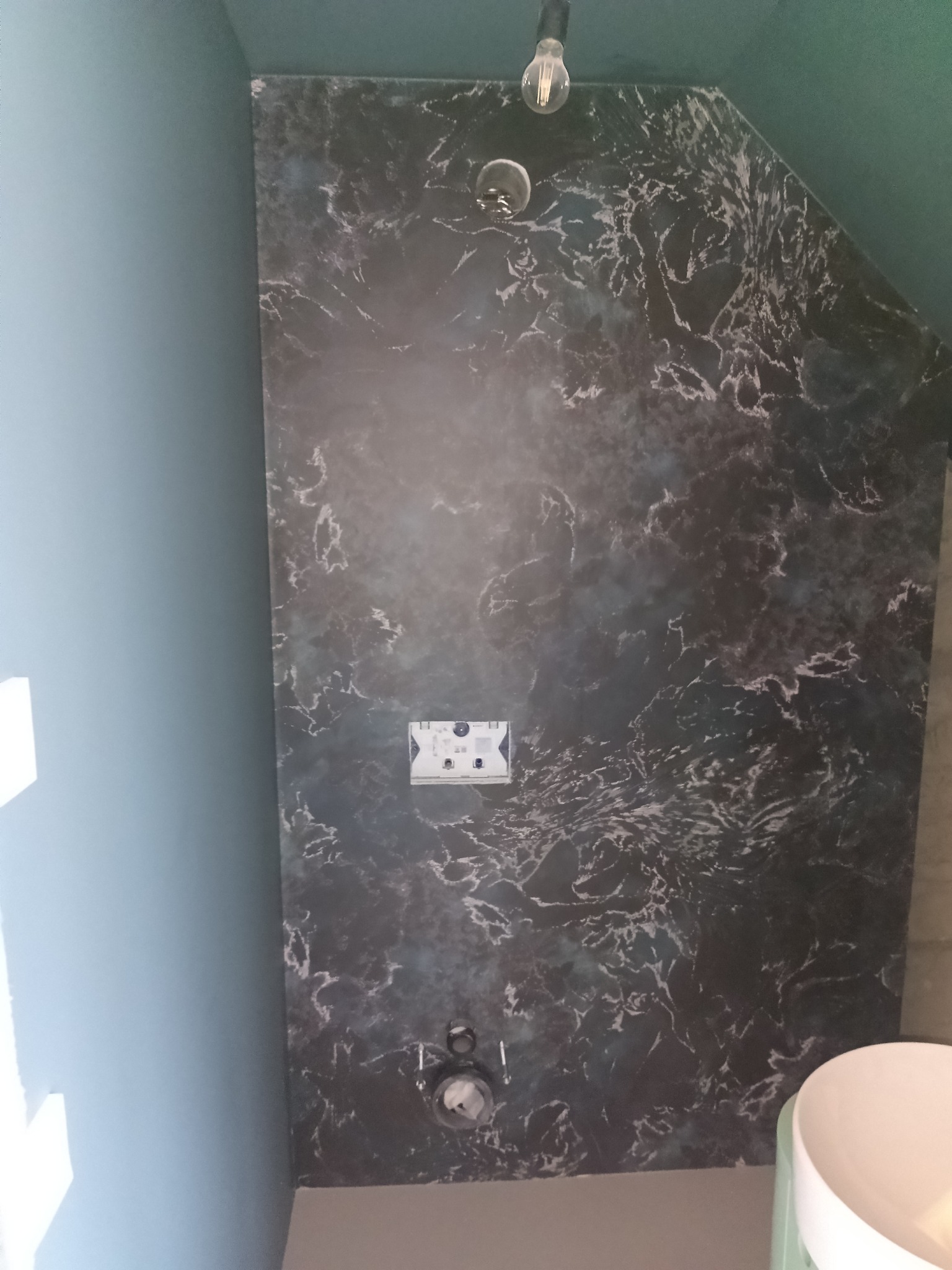 Ściana z efektem marmuru w łazience, widoczna instalacja elektryczna i fragment umywalki. Dekoracyjne wykończenie wnętrza, nowoczesny design.