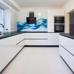 Wojciech Raś Twój Wymiar Pracownia Mebli - Nowoczesna, biała kuchnia z czarnymi blatami i abstrakcyjnym panelem szklanym. Minimalistyczny design, jasne płytki podłogowe, wbudowane sprzęty AGD.