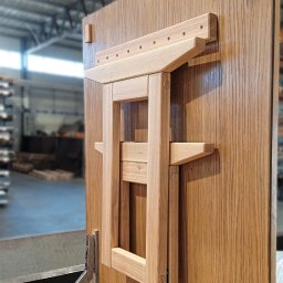 Wojciech Raś Twój Wymiar Pracownia Mebli - Drewniany, składany stół przymocowany do płyty meblowej z widocznymi okuciami. Jasne drewno, minimalistyczny design, widok z boku, warsztatowe tło.