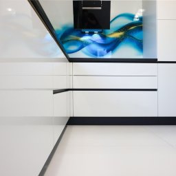 Wojciech Raś Twój Wymiar Pracownia Mebli - Biała, nowoczesna kuchnia z połyskiem, minimalistyczne fronty szafek, czarne akcenty, abstrakcyjny panel nad blatem, wbudowane sprzęty AGD.