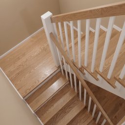 Twój Wymiar Pracownia Mebli - Jasne, drewniane schody z białymi balustradami, widok z góry. Naturalne oświetlenie podkreśla strukturę drewna. Minimalistyczny design.