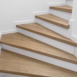 Twój Wymiar Pracownia Mebli - Jasne, drewniane stopnie schodów z białymi podstopnicami, widziane z dołu pod kątem. Minimalistyczny design, nowoczesne wykończenie.