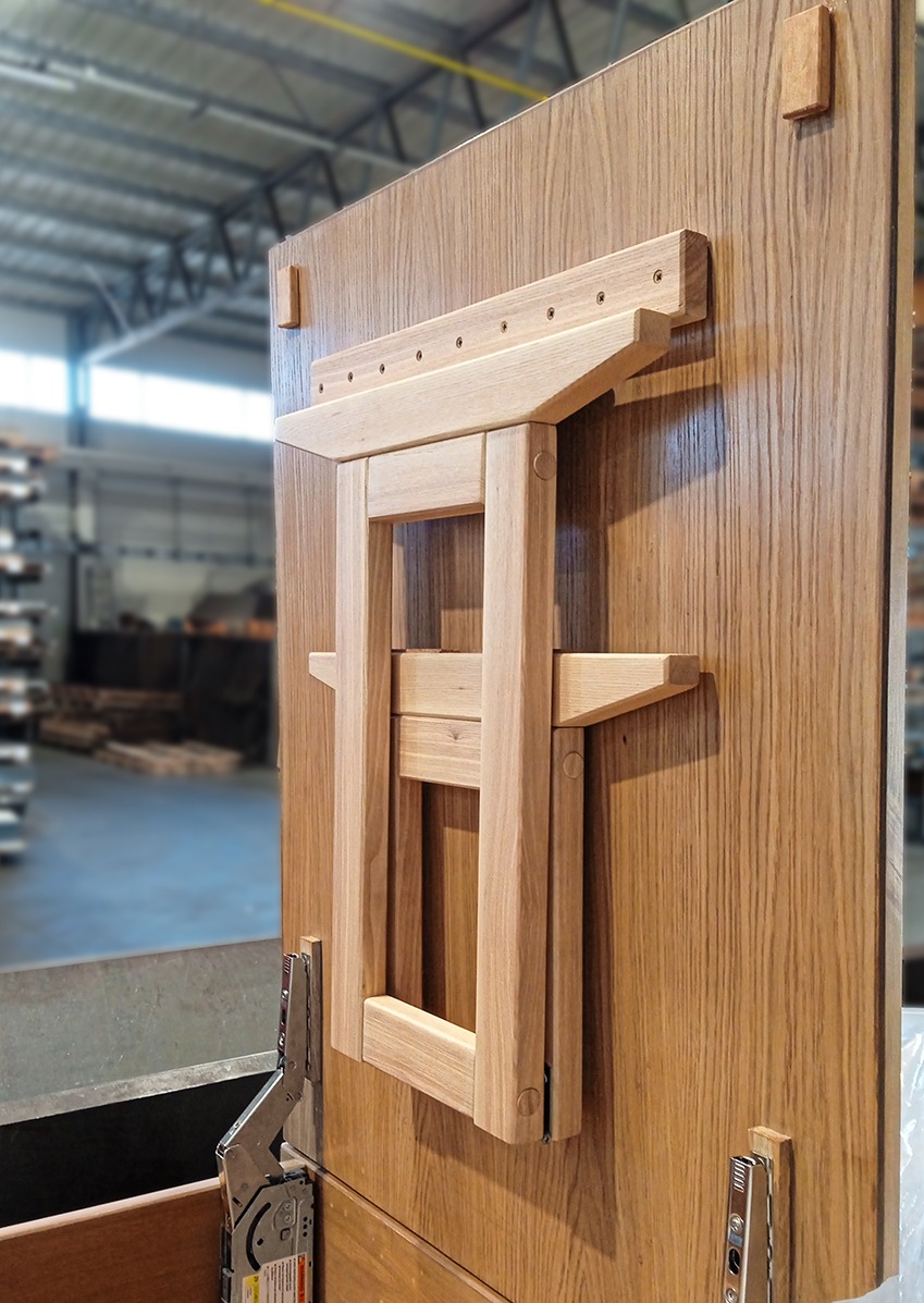 Drewniany, składany stół przymocowany do płyty meblowej z widocznymi okuciami. Jasne drewno, minimalistyczny design, widok z boku, warsztatowe tło.