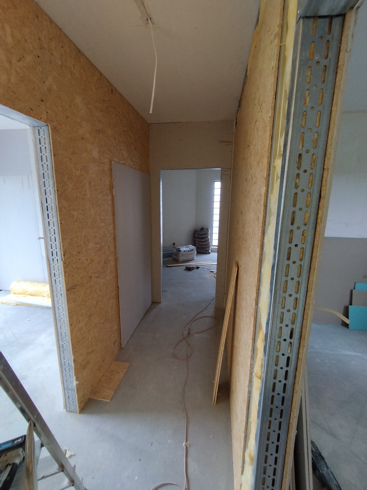 Wnętrze w trakcie prac wykończeniowych: ściany z płyt OSB i metalowych profili, widoczne materiały izolacyjne i płyty gipsowe. Surowy stan, przygotowanie do dalszych prac.