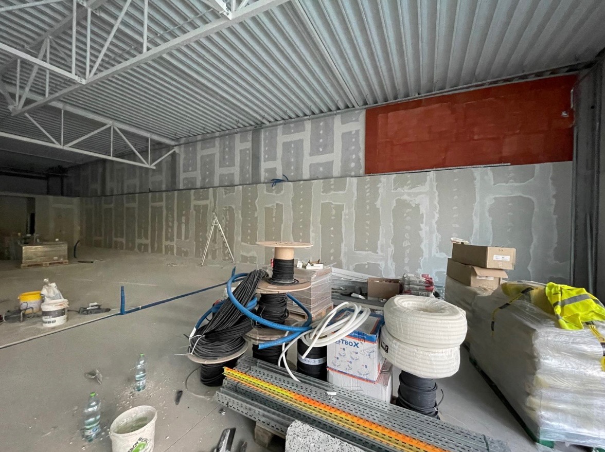 Wnętrze w trakcie prac wykończeniowych: ściany z płyt karton-gips, widoczne kable, profile i narzędzia. Fragment ściany pomalowany na czerwono. Metalowa konstrukcja sufitu.