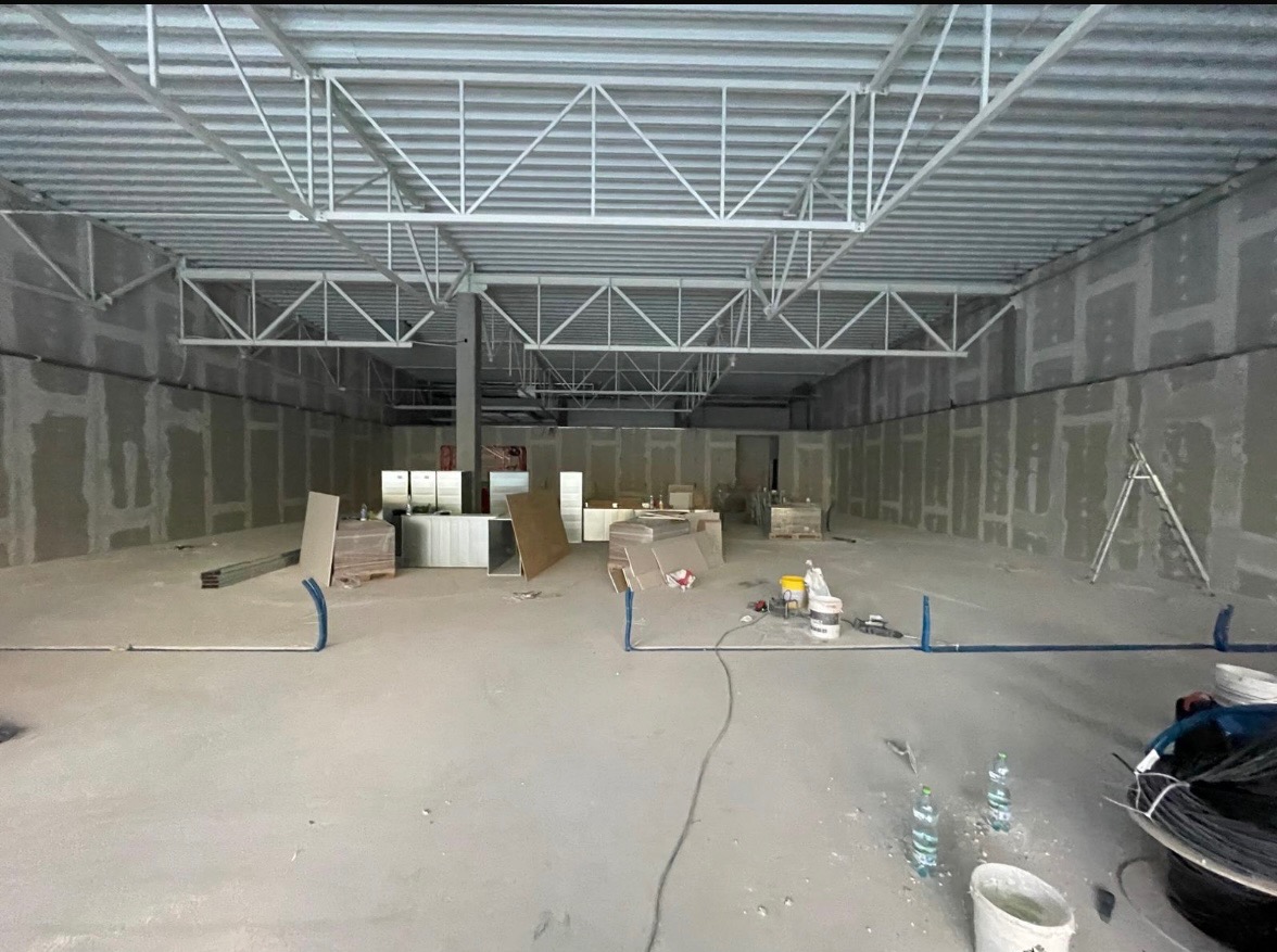 Wnętrze hali w trakcie prac wykończeniowych: ściany z płyt karton-gips, widoczne profile, drabina, materiały budowlane. Stalowa konstrukcja dachu. Surowy stan.