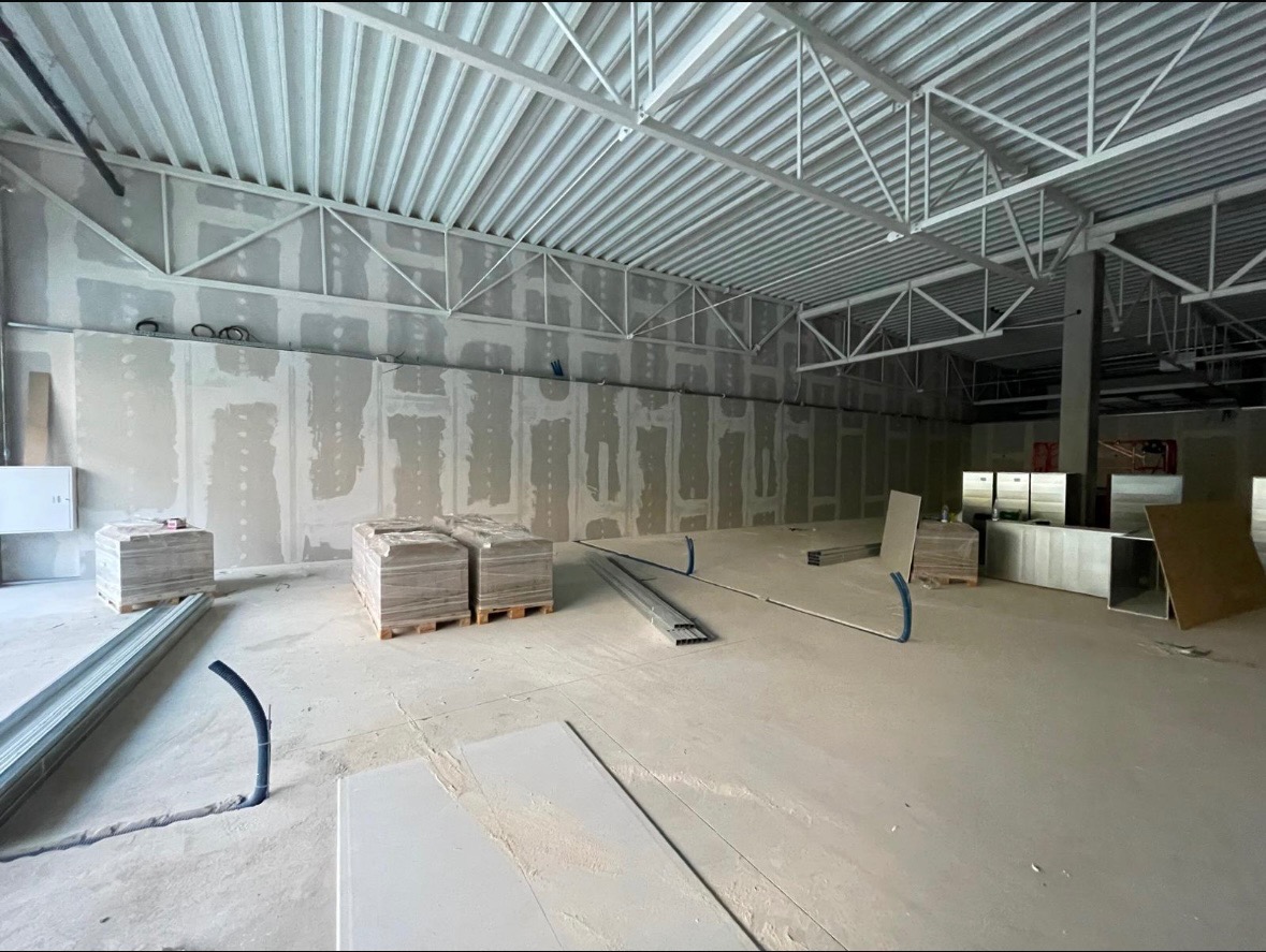 Wnętrze w trakcie prac wykończeniowych: ściany z płyt karton-gips, widoczne profile i palety z materiałami. Surowy stan, przygotowanie do dalszych etapów.