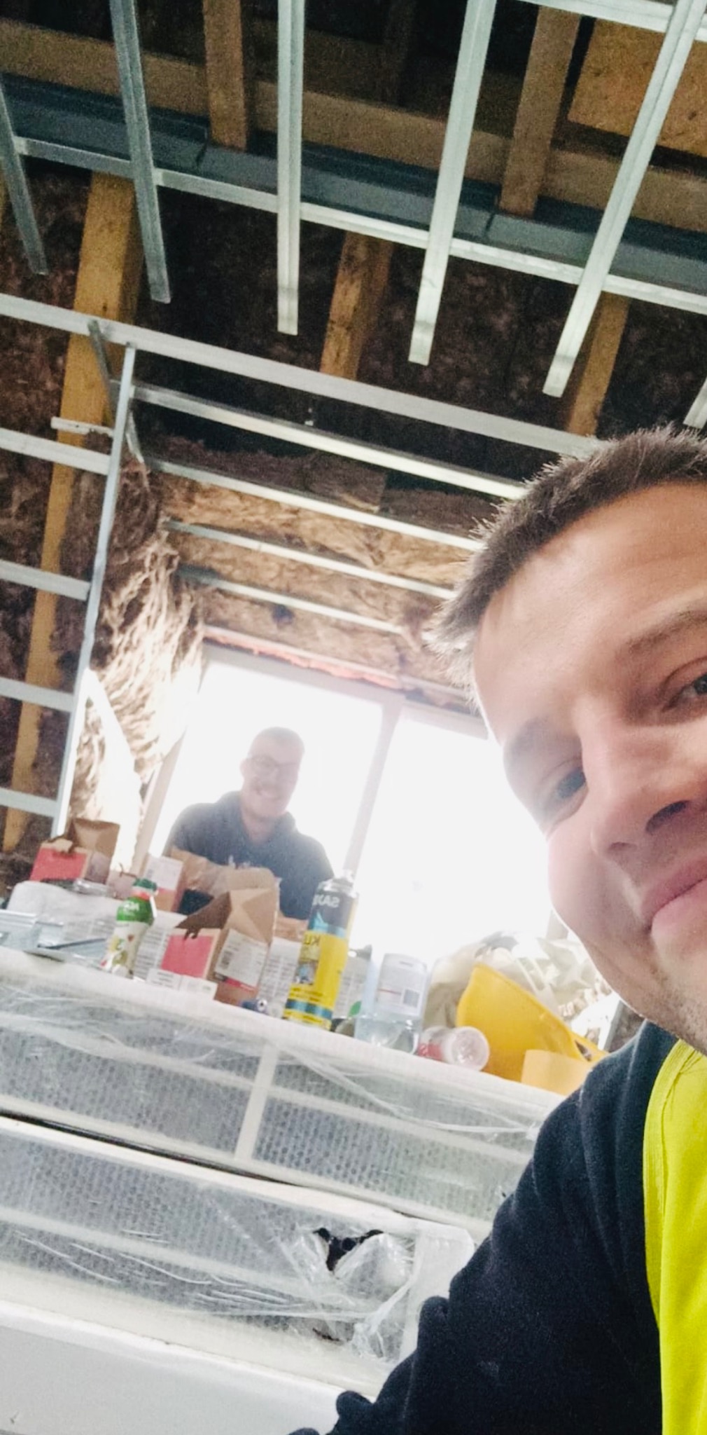 Montaż sufitu z płyt karton-gips: widok z dołu na konstrukcję metalową, izolację z wełny mineralnej i dwóch monterów podczas pracy. Ujęcie z bliska, z perspektywy jednego z nich.