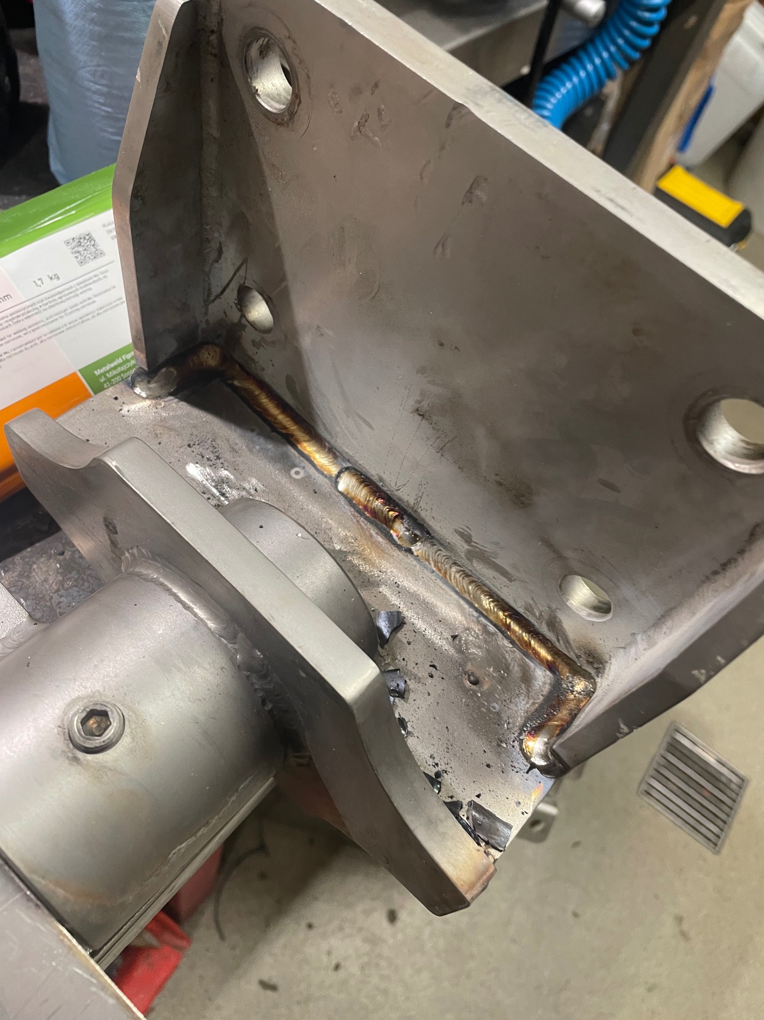 Szlifowana, metalowa konstrukcja spawana z widocznymi śladami obróbki i spoinami. Element z otworami montażowymi, wykonany z dbałością o detale.