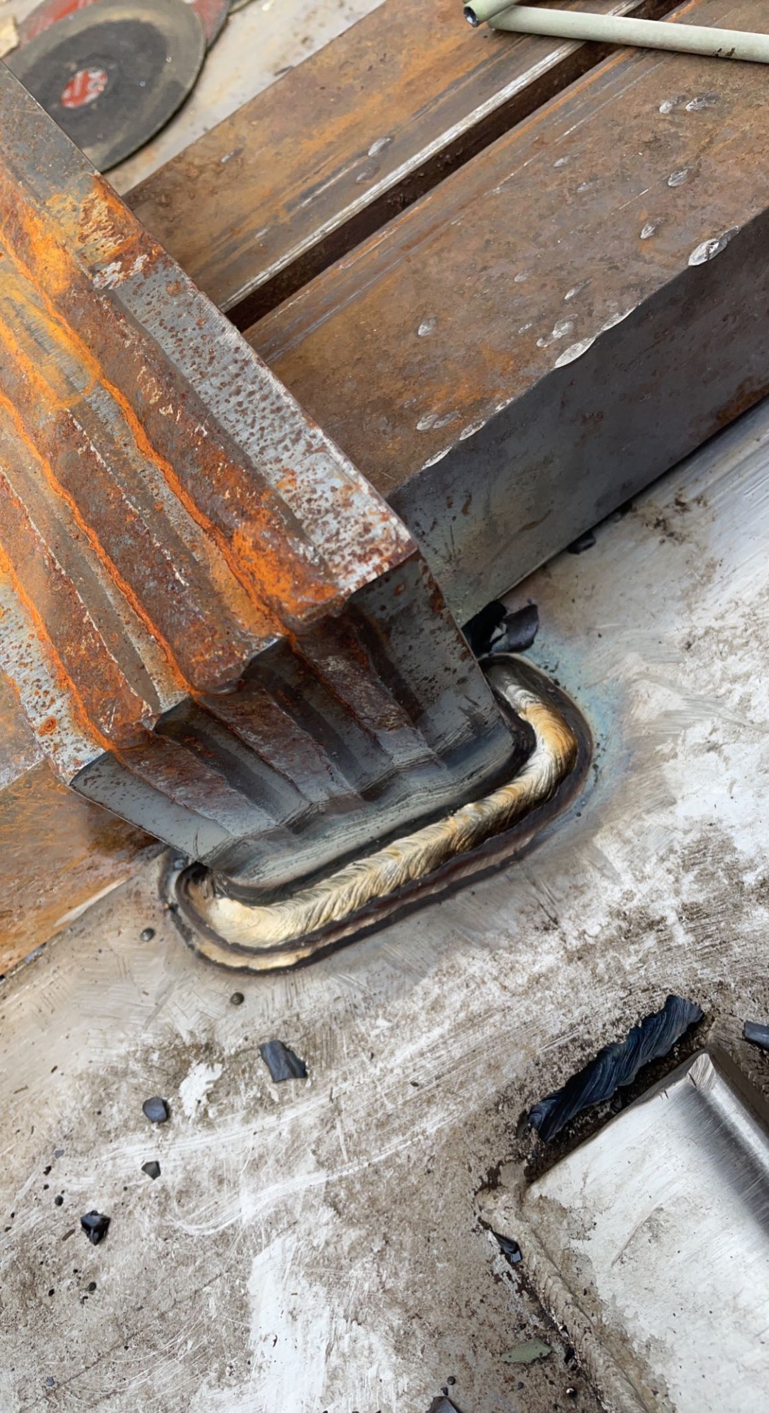 Spoina łącząca zardzewiałe, stalowe profile pod kątem prostym. Widoczne ślady obróbki i zabrudzenia na powierzchni metalu. Detal spawalniczy z bliska.