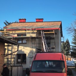 Usługi dekarskie Nowakowski - Dom w trakcie wymiany dachu, widoczne rusztowania, częściowo zdjęte stare pokrycie i czerwone kominy. Na pierwszym planie czerwony samochód dostawczy.