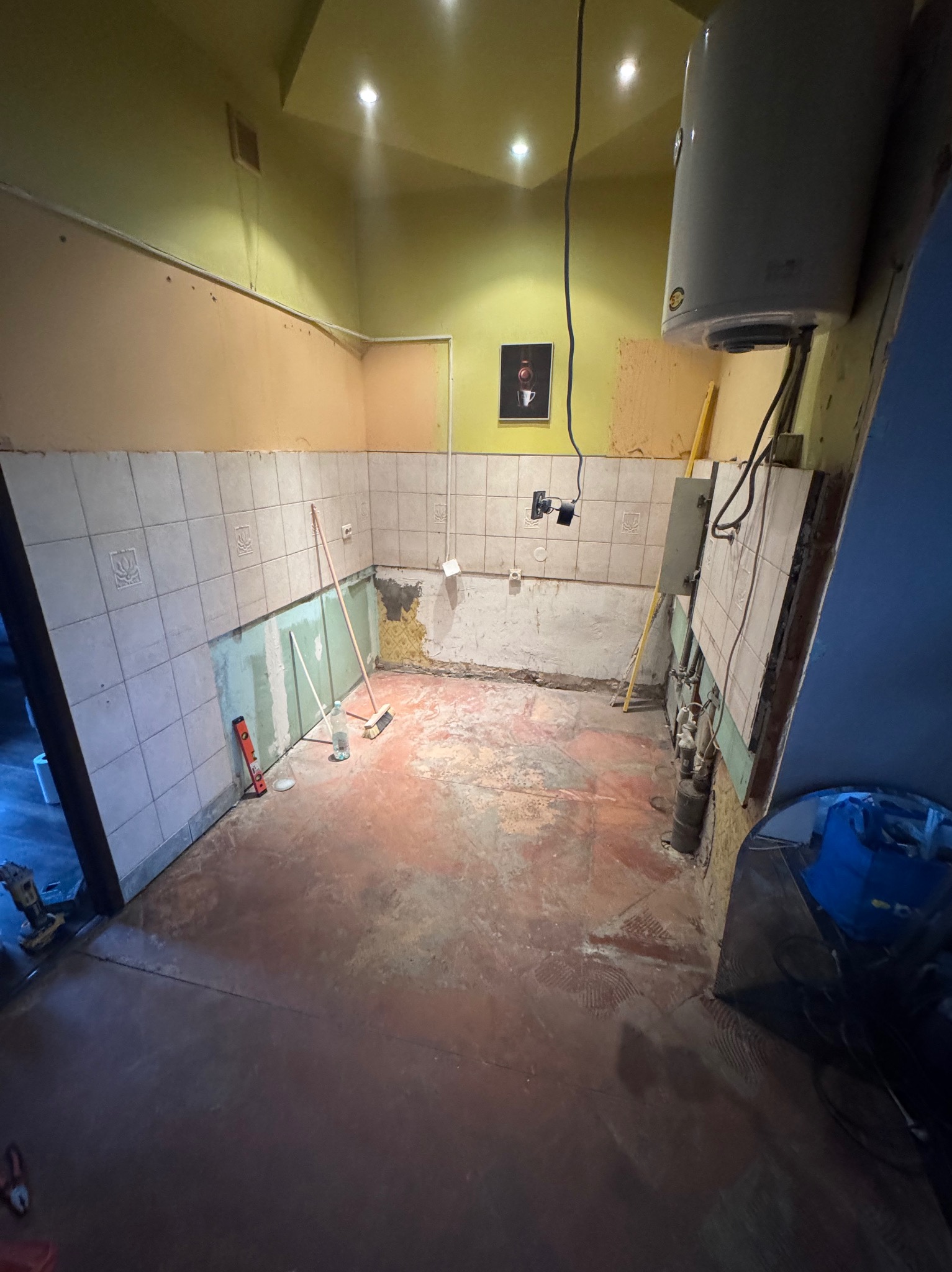 Demontaż płytek w kuchni przed remontem. Widoczne narzędzia, fragmenty odspojonych płytek i przygotowane podłoże. Ujęcie z perspektywy wejścia do pomieszczenia.