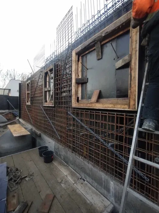 Zbrojenie ściany z otworami okiennymi, szalunki drewniane, siatka zbrojeniowa, drabina, etap budowy, widok z dołu.
