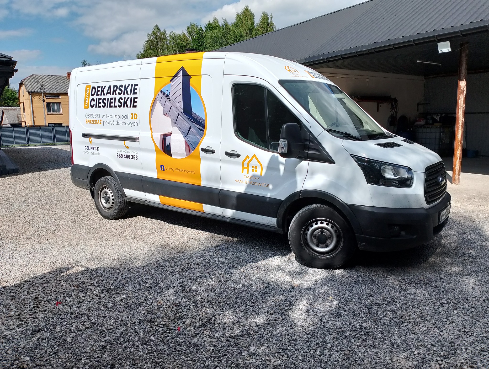 Biały van z żółtymi akcentami i grafiką dachu, zaparkowany na żwirowym podłożu. Reklama usług dekarsko-ciesielskich z adresem i numerem telefonu.