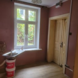 Tadeusz De - Pokój przed malowaniem: różowe ściany, okno z widokiem na zieleń, umywalka i dwa wiadra z farbą. Widoczne ślady wcześniejszych prac remontowych.