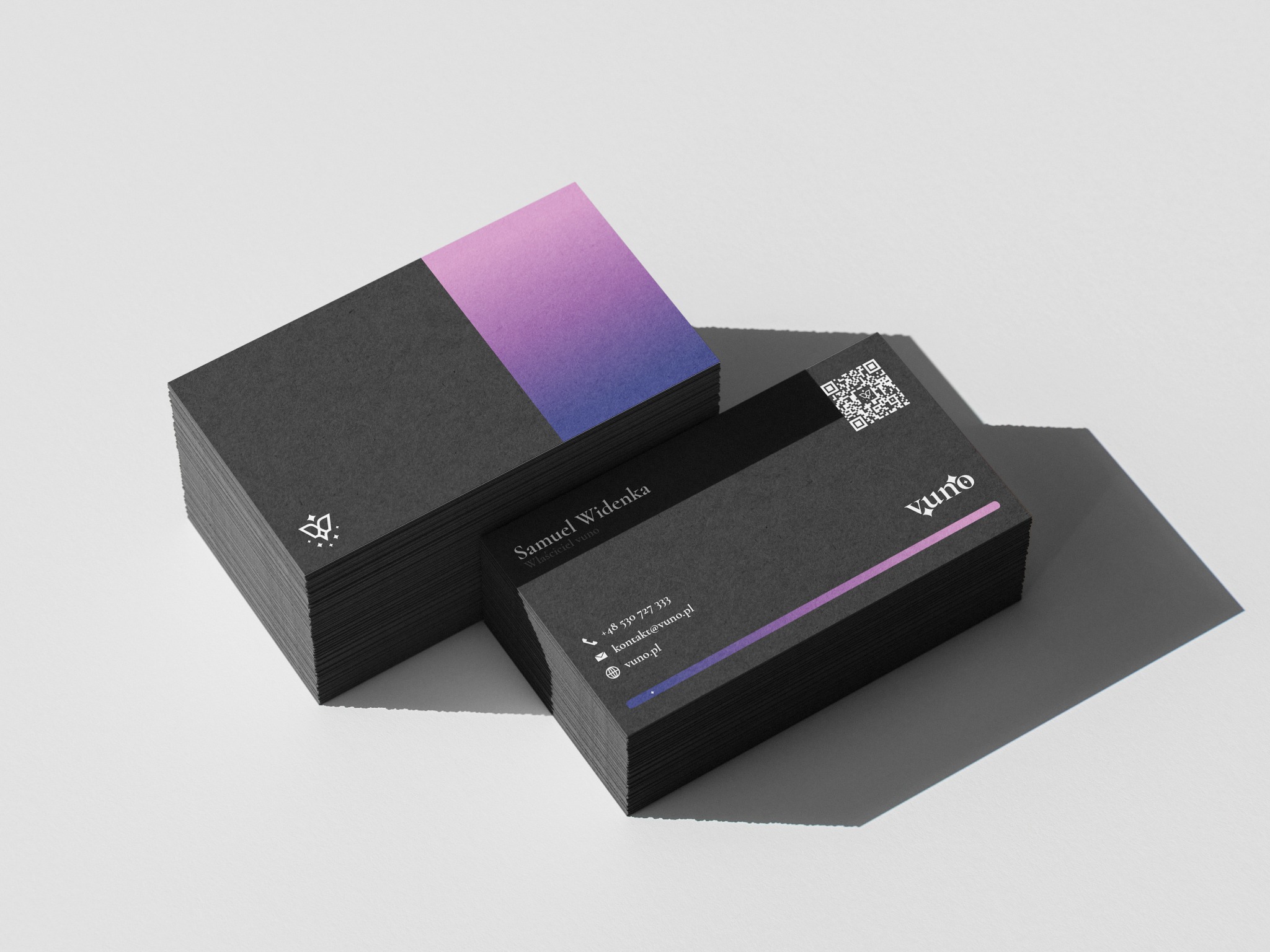 Stos czarnych wizytówek z gradientem fioletowo-różowym i danymi kontaktowymi na jasnym tle. Minimalistyczny design, ostre cienie, nowoczesny styl.