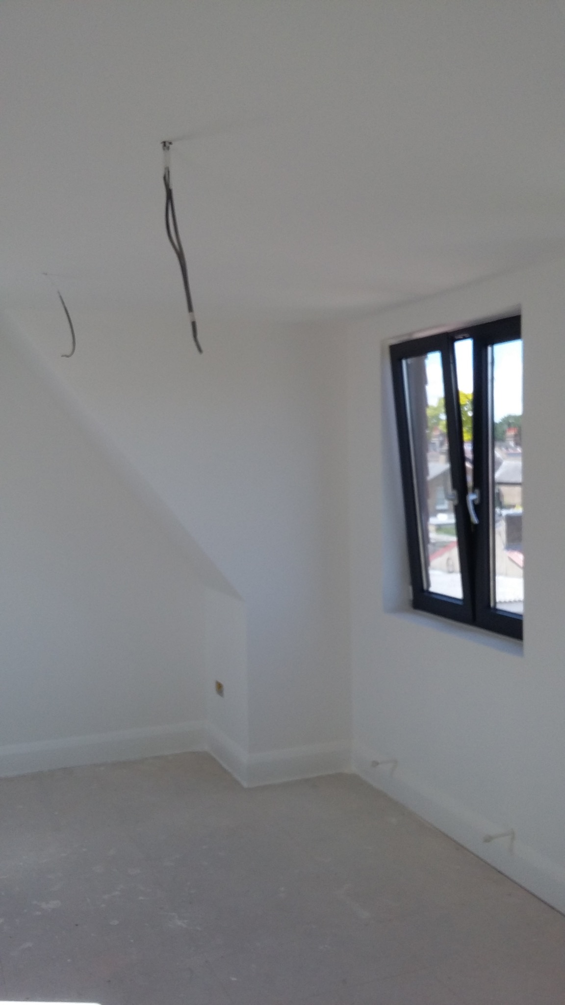 Wnętrze pokoju po szpachlowaniu i malowaniu na biało, z czarnym oknem i wystającymi kablami z sufitu. Widoczne listwy przypodłogowe i skos dachu.