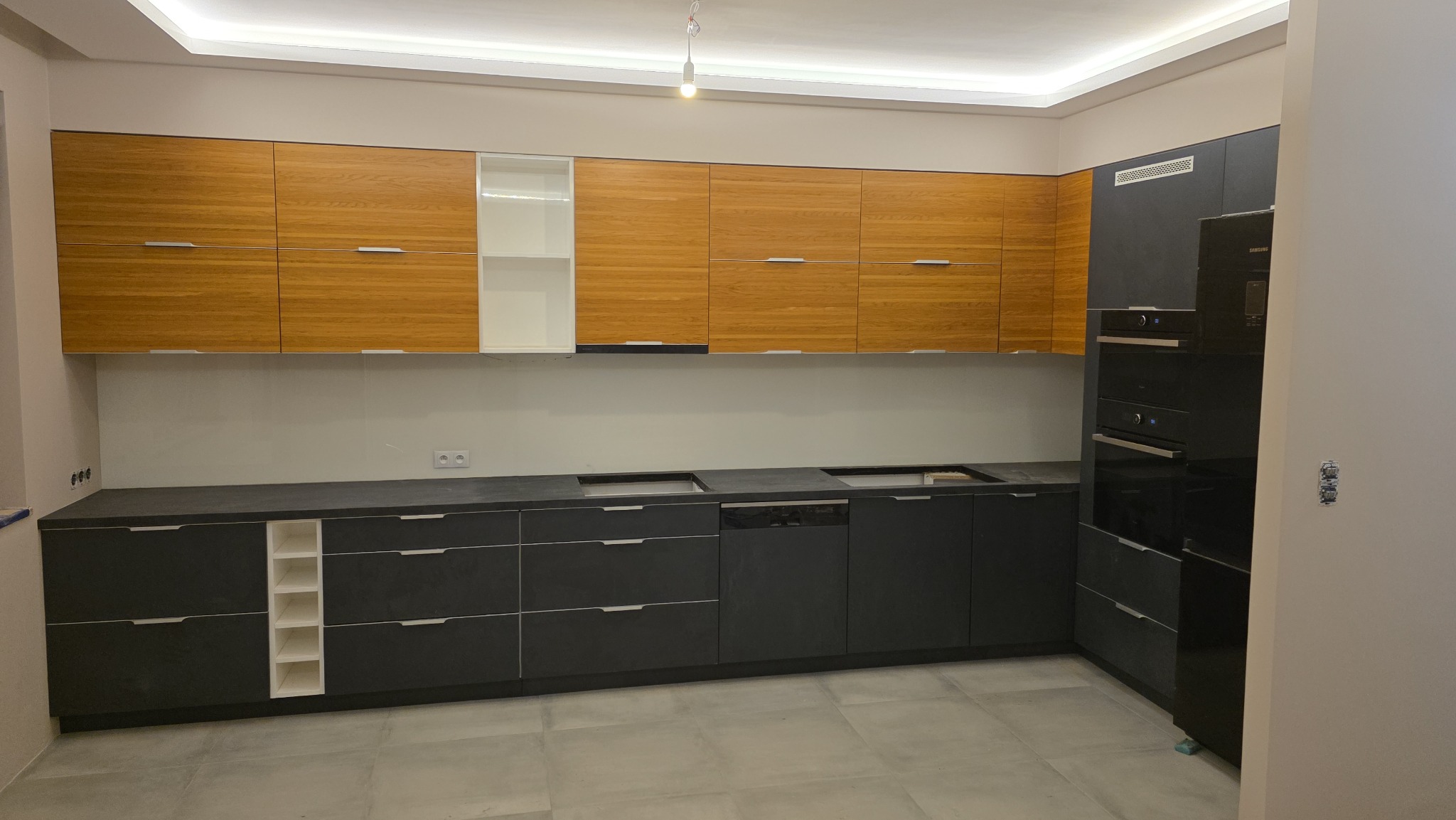 Nowoczesna kuchnia z drewnianymi szafkami górnymi i grafitowymi dolnymi, z wbudowanym sprzętem AGD i oświetleniem LED podszafkowym. Minimalistyczny design.