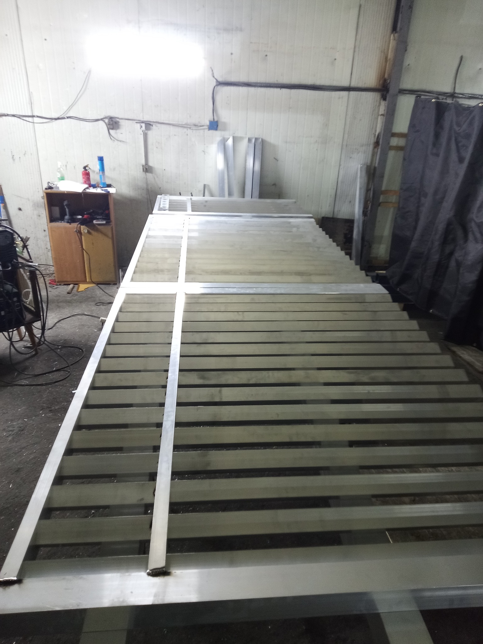 Konstrukcja metalowa z profili, prawdopodobnie element bramy wjazdowej, w warsztacie. Widoczne spawy i surowy metal. Ujęcie z perspektywy.