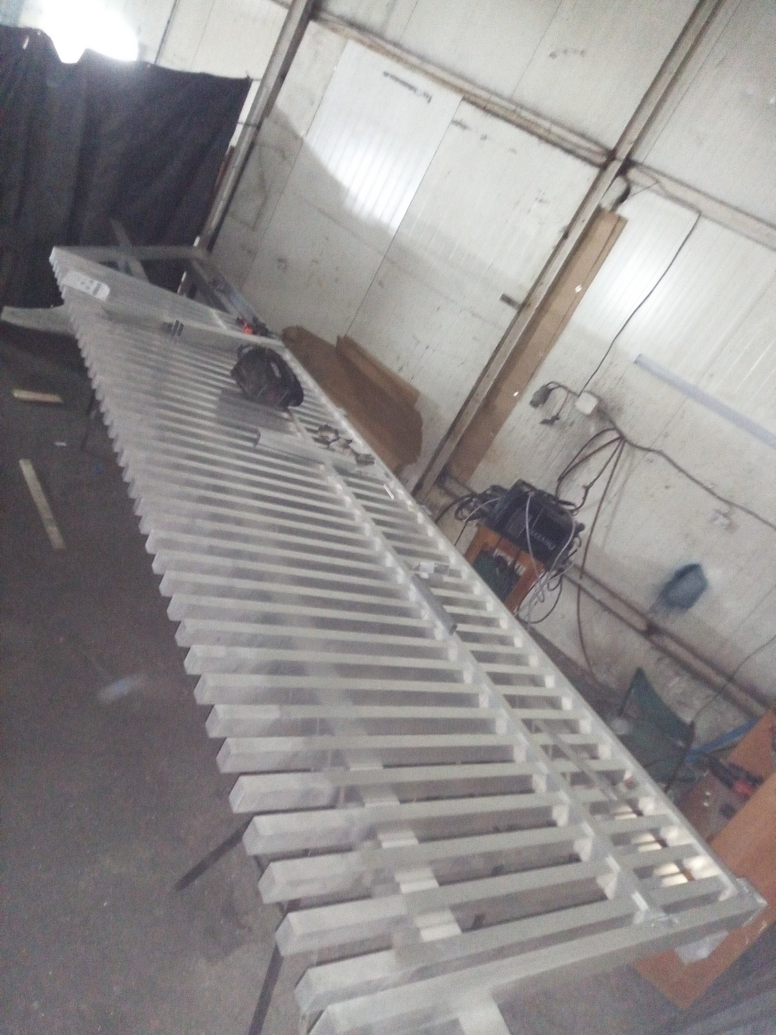 Metalowa konstrukcja w warsztacie, prawdopodobnie element ogrodzenia lub bramy, w trakcie produkcji. Widoczne narzędzia i materiały ślusarskie.