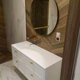 Bak-Pol Baka Krzysztof - Nowoczesna łazienka: biała szafka z umywalką i złotymi uchwytami, owalne lustro z podświetleniem, wzorzyste płytki na ścianie i marmurowa podłoga.