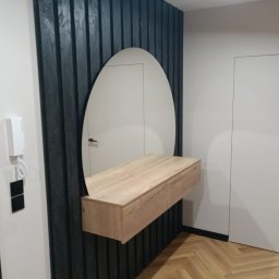 Bak-Pol Baka Krzysztof - Nowoczesna aranżacja przedpokoju: owalne lustro z drewnianą konsolą na tle ściany z ciemnych, pionowych paneli. Parkiet w jodełkę, minimalistyczne drzwi i oświetlenie.