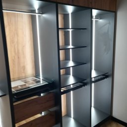 Bak-Pol Baka Krzysztof - Nowoczesna, otwarta garderoba z szarymi półkami, drewnianymi elementami i oświetleniem LED. Widoczne szuflady i półki na akcesoria. Podłoga parkiet.