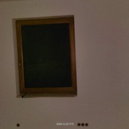 Bak-Pol Baka Krzysztof - Ściana po malowaniu z drewnianym oknem. Widoczne ślady po gniazdkach elektrycznych. Świeżo pomalowane wnętrze w neutralnym odcieniu.