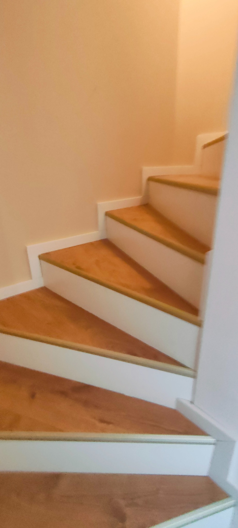 Drewniane schody z białymi podstopnicami i listwami przypodłogowymi, widok z dołu, ciepłe oświetlenie, ukończony remont.