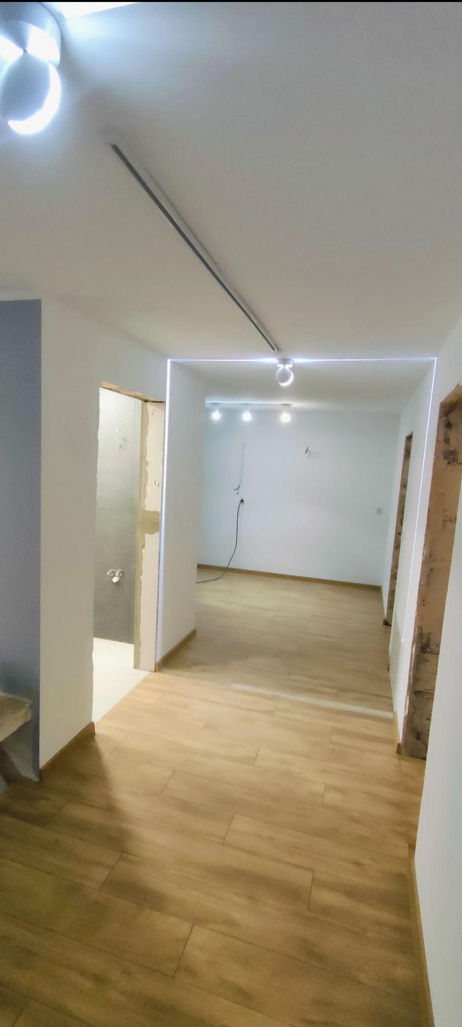 Jasne, odnowione wnętrze z drewnopodobną podłogą i nowoczesnym oświetleniem LED. Widoczne fragmenty ścian w trakcie prac wykończeniowych.