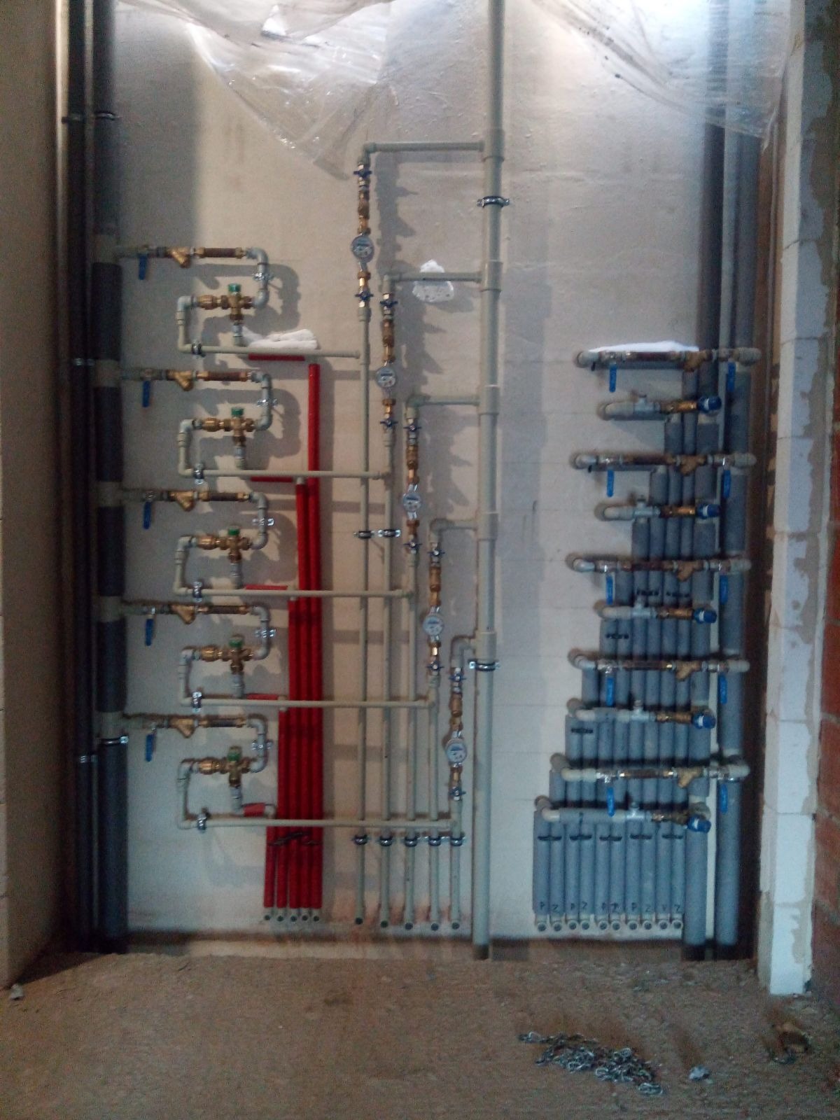 Szczegółowe ułożenie instalacji grzewczej z rur i zaworów na ścianie w surowym wnętrzu. Widoczne pionowe i poziome rury, liczniki oraz elementy mocujące.