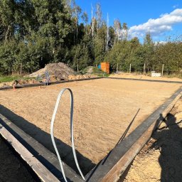 Mix-Bud - Przygotowany teren pod fundamenty domu z widocznym szalunkiem i izolacją, na tle zieleni i błękitnego nieba. Widoczny cień osoby.