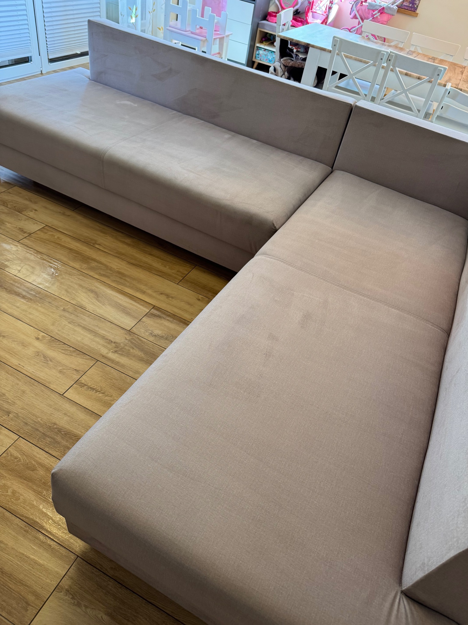 Narożnik z jasną tapicerką na drewnianej podłodze, widok z góry. W tle dziecięcy pokój. Usługa prania kanap w Białystoku.