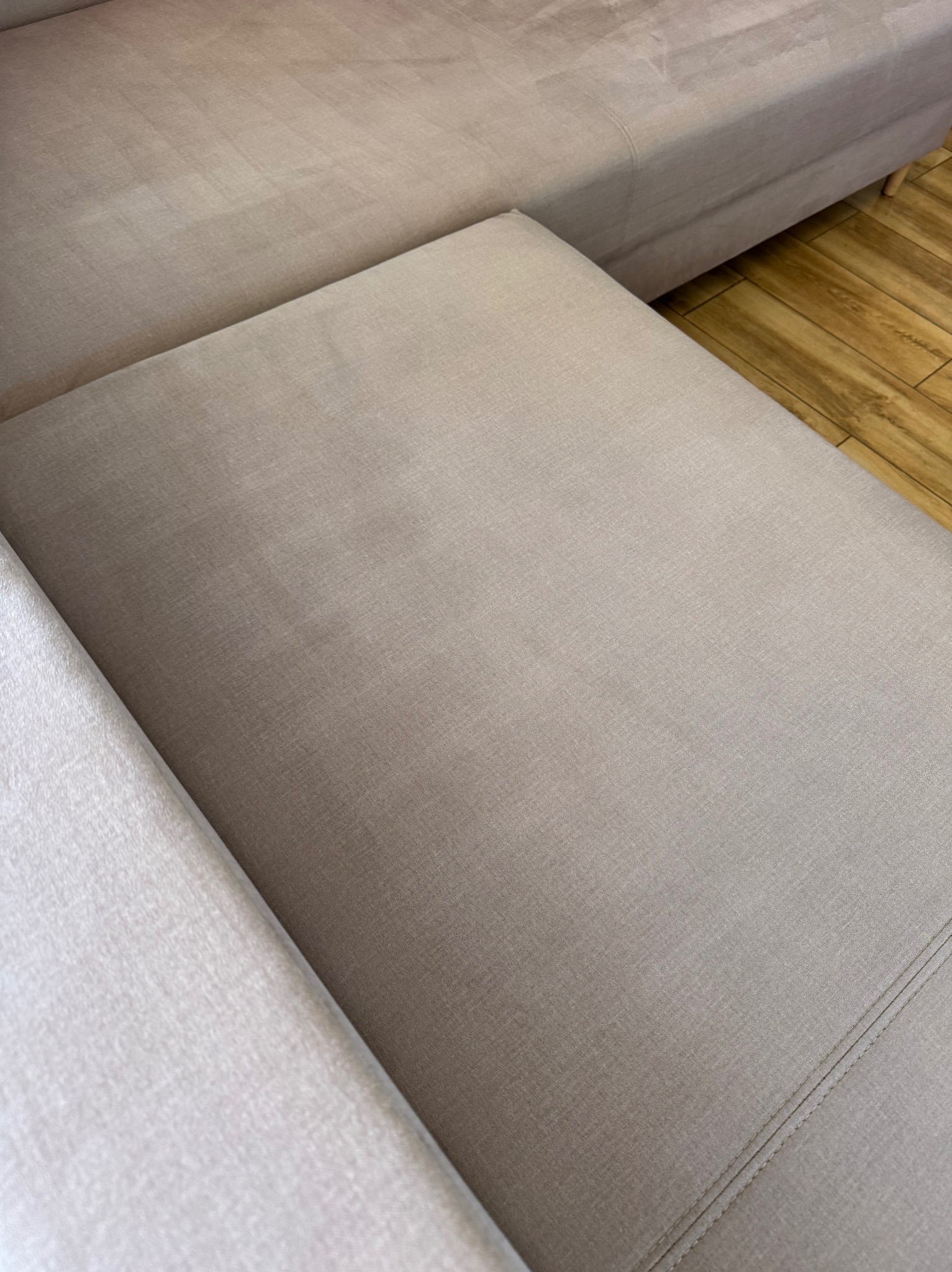 Jasny narożnik z beżową tapicerką, widoczny z bliska, z drewnianą podłogą w tle. Minimalistyczny design, czyste linie i gładka powierzchnia tkaniny.