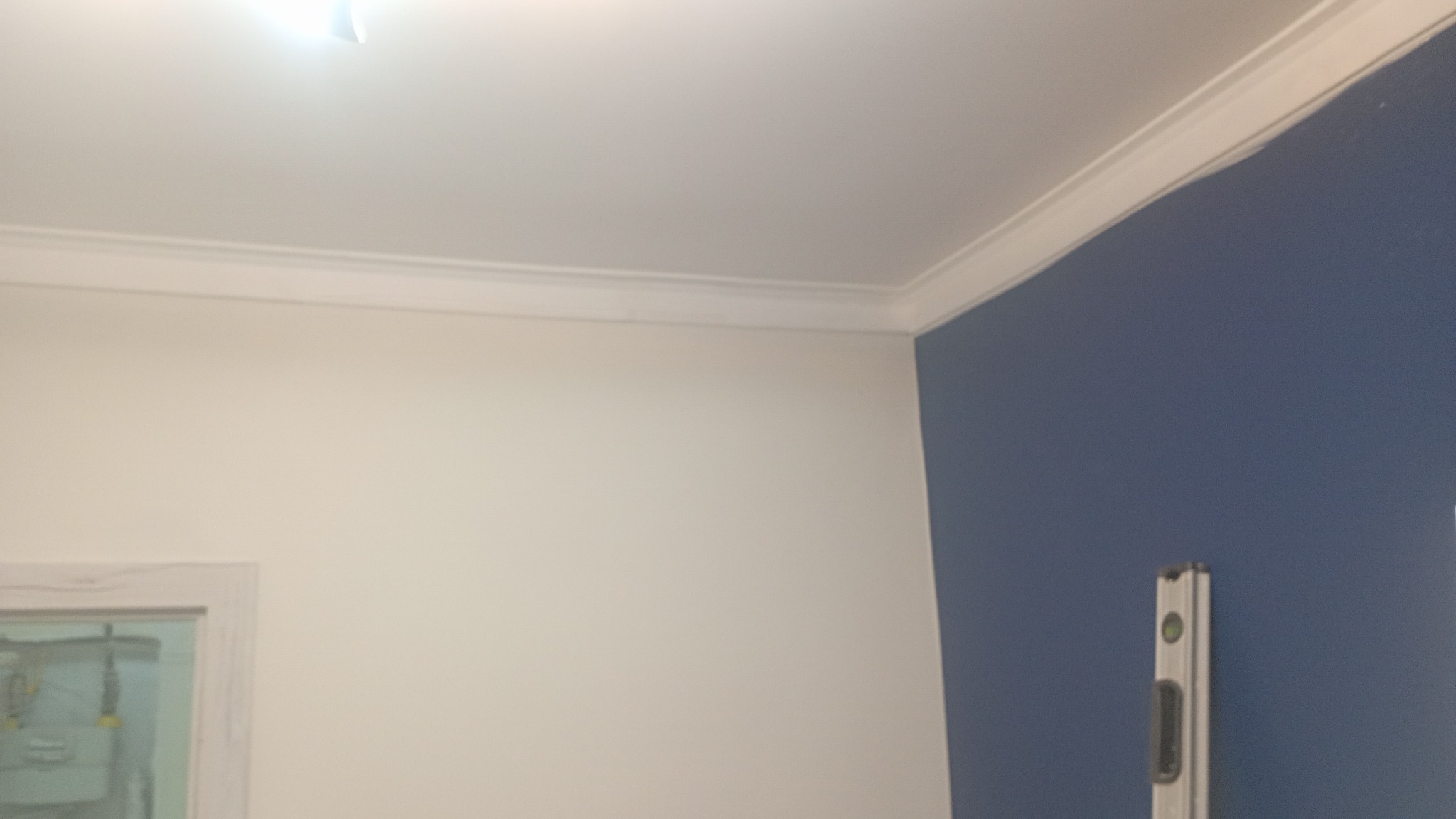 Biała ściana z listwą przysufitową i fragmentem niebieskiej ściany z poziomicą. Widoczny fragment okna.