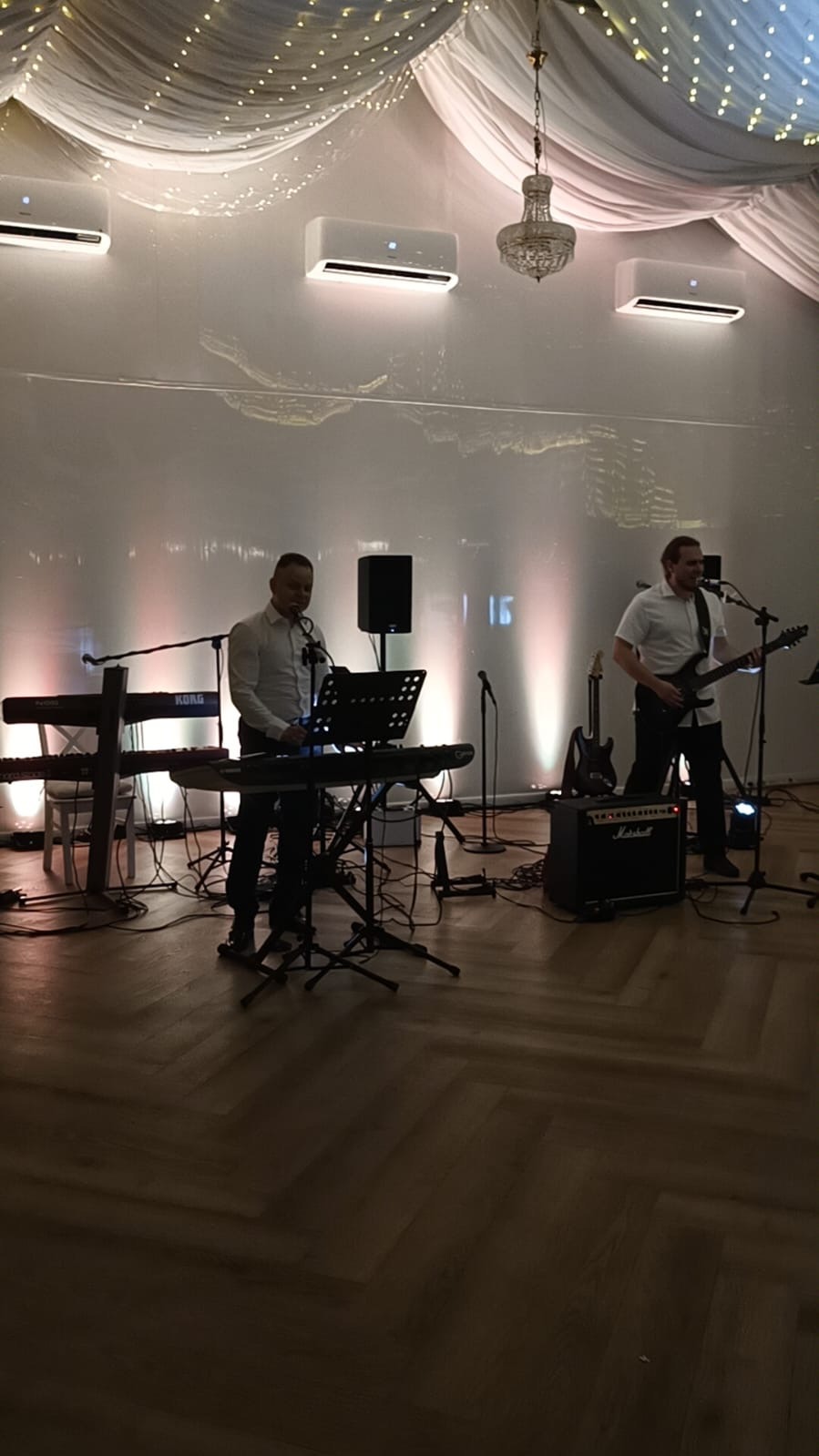 Zespół muzyczny na scenie z klawiszami Korg i gitarą elektryczną Marshall, oświetlenie sceniczne i dekoracje sufitowe tworzą klimat imprezy.