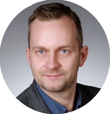 Portret biznesowy mężczyzny w Koninie, z krótkimi włosami i niebieską koszulą, na szarym tle. Profesjonalny wizerunek CEO firmy IT.