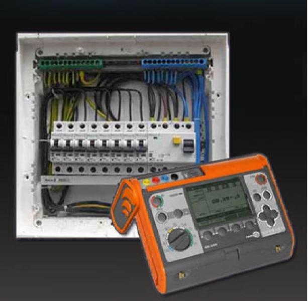 Rozdzielnica elektryczna z zainstalowanymi bezpiecznikami i przewodami, obok leży miernik elektryczny w obudowie pomarańczowo-szarej.