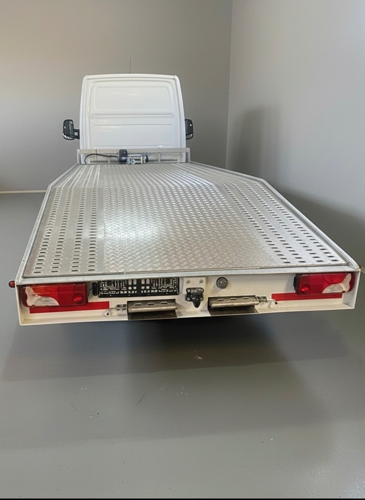 Widok z tyłu białej lawety z metalową, diamentową platformą. Widoczne światła, tablica rejestracyjna i elementy mocujące. Szare tło.