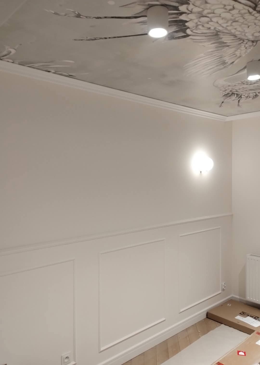 Eleganckie wykończenie wnętrza: białe ściany z dekoracyjnymi panelami, ozdobny sufit z motywem ptaków, nowoczesne oświetlenie punktowe i listwy przypodłogowe.